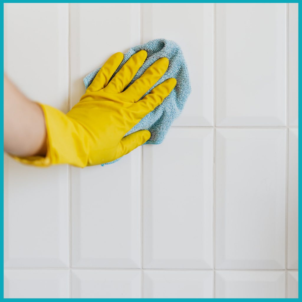 A gloved hand cleans a tiled shower stall.